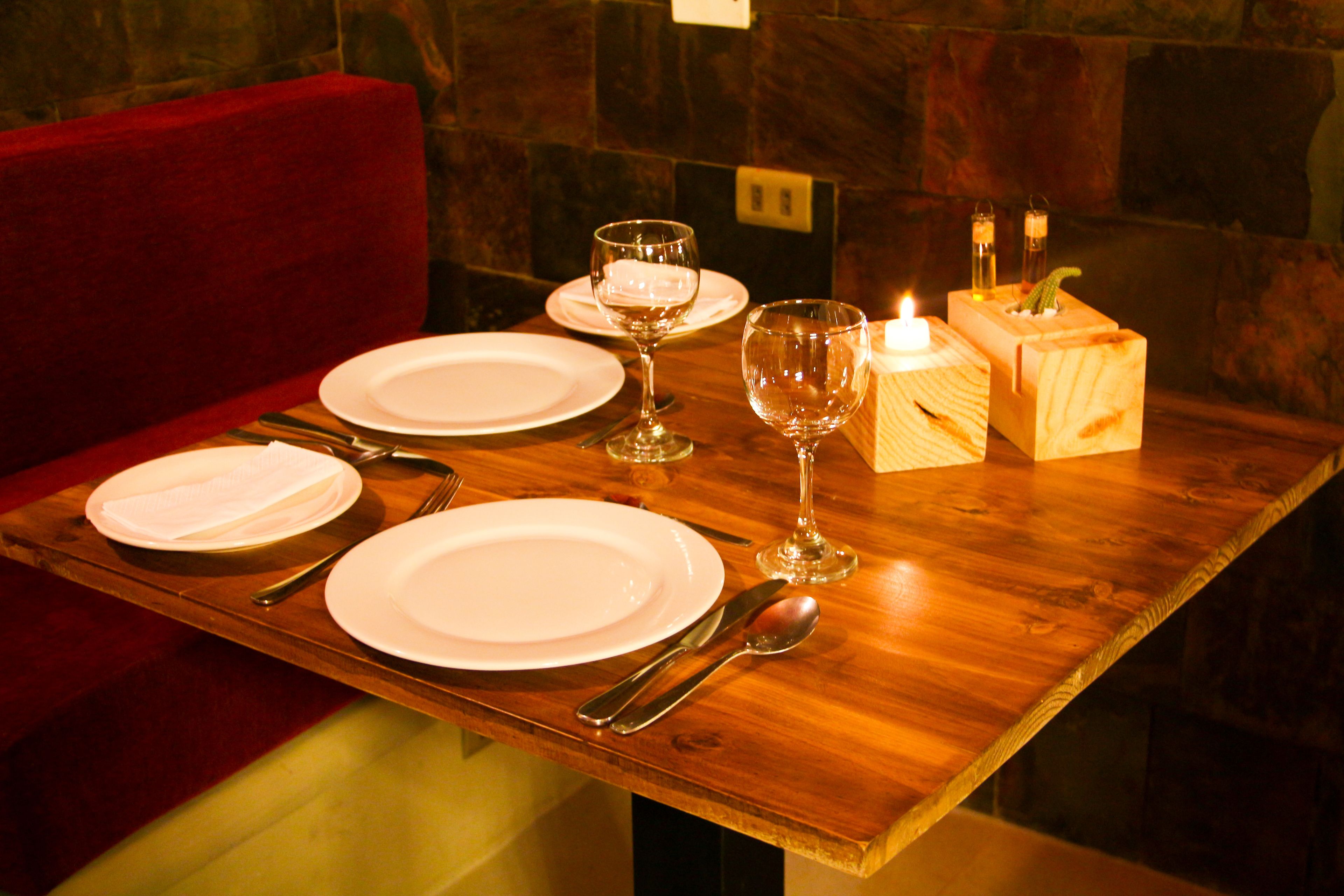Un tavolo da pranzo in legno apparecchiato con piatti bianchi, posate e bicchieri da vino, con candele in un portacandele in legno.