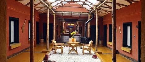 A corridor with wooden pillars, a central seating area with a table and chairs, and a television screen at the end.