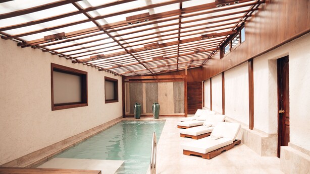 A swimming pool with wooden deck chairs, a wooden ceiling, and a tiled floor.