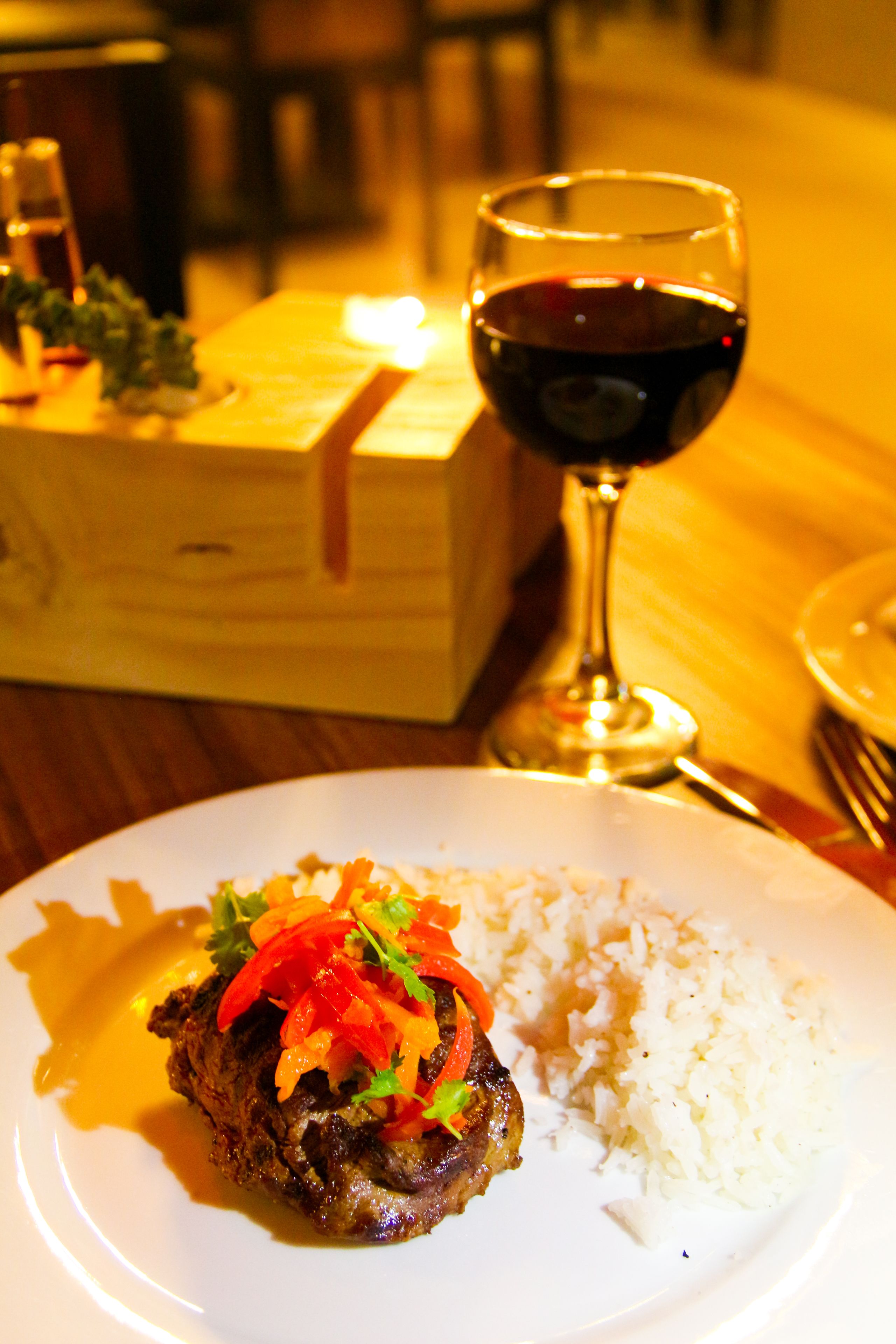 A plate with a meat dish, rice, and a glass of red wine on a wooden table.