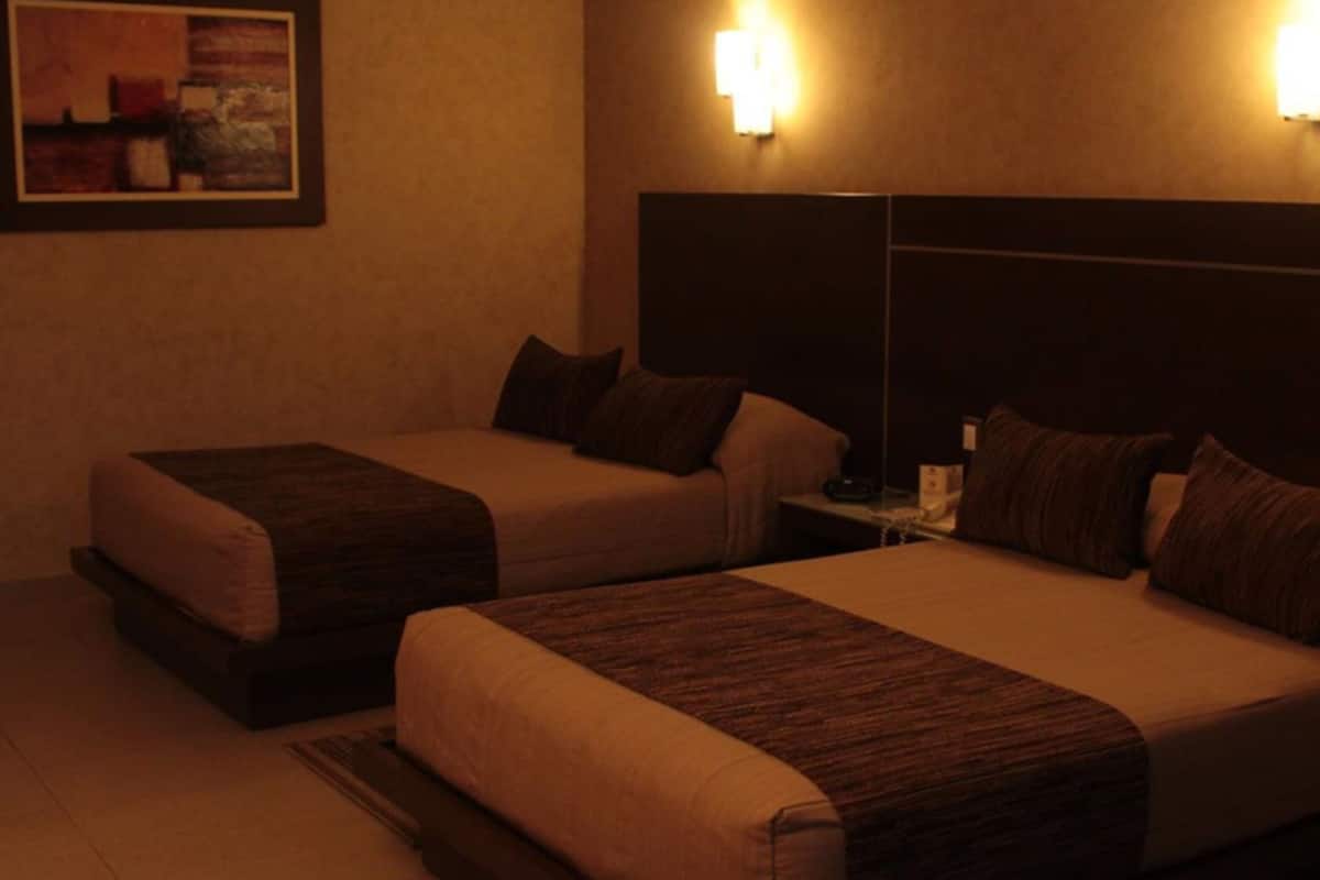 Habitación de hotel con dos camas, una mesita de noche y una lámpara fijada en la pared.