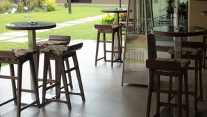 An outdoor patio area with round tables and wooden stools, a glass door leading to a covered entrance, and a sign reading "BAR". - Layfer Express Cordoba Veracruz Mexico (Córdoba)