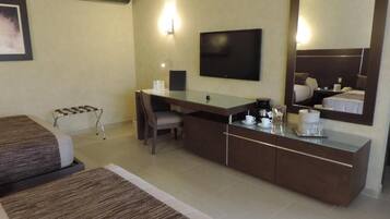 Habitación de hotel con cama, escritorio, silla, televisión, espejo y cafetera.