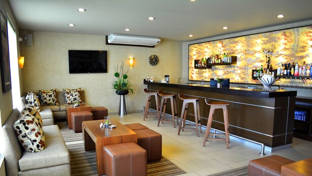 A modern bar area with stools, a sofa with patterned cushions, and a television mounted on the wall. - Layfer Express Cordoba Veracruz Mexico (Córdoba)