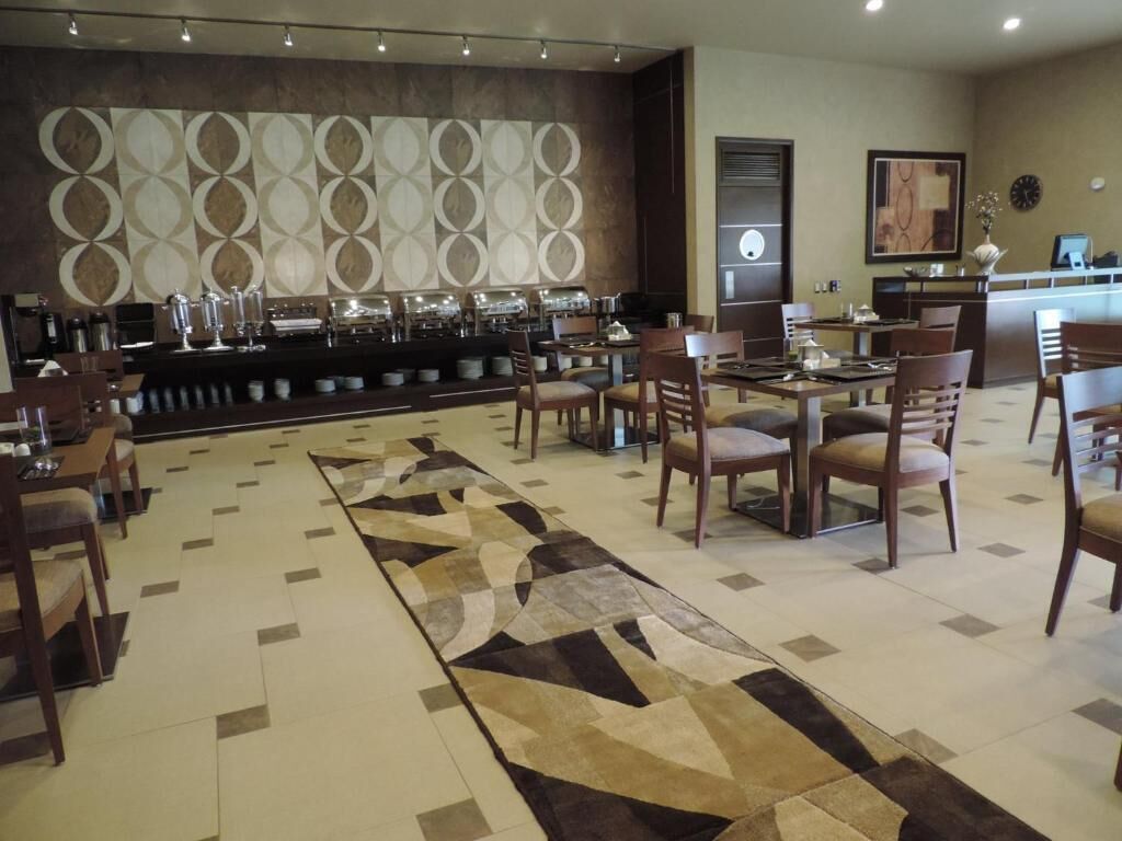 Un vestíbulo de hotel con una zona de bar, varios conjuntos de asientos y una alfombra estampada.