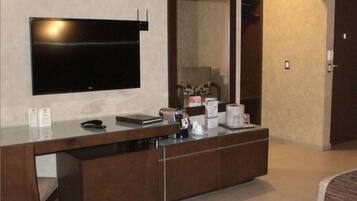 Una habitación de hotel moderna con un televisor de pantalla plana grande montado en la pared, una mesita de madera con cafetera y un espejo grande.