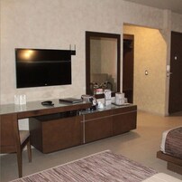 Una habitación de hotel moderna con un televisor de pantalla plana grande montado en la pared, una mesita de madera con cafetera y un espejo grande.