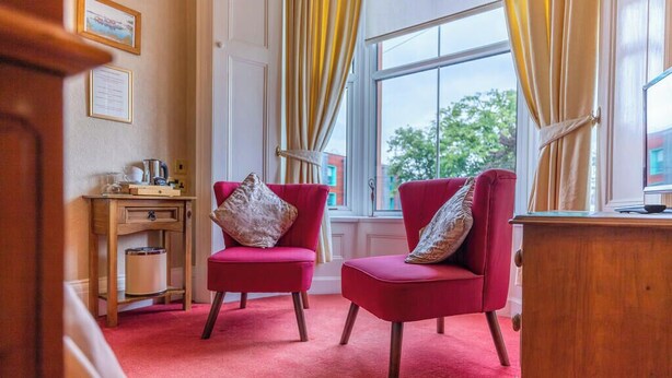 Una habitación con dos sillas rojas, un escritorio de madera y una ventana con cortinas amarillas.