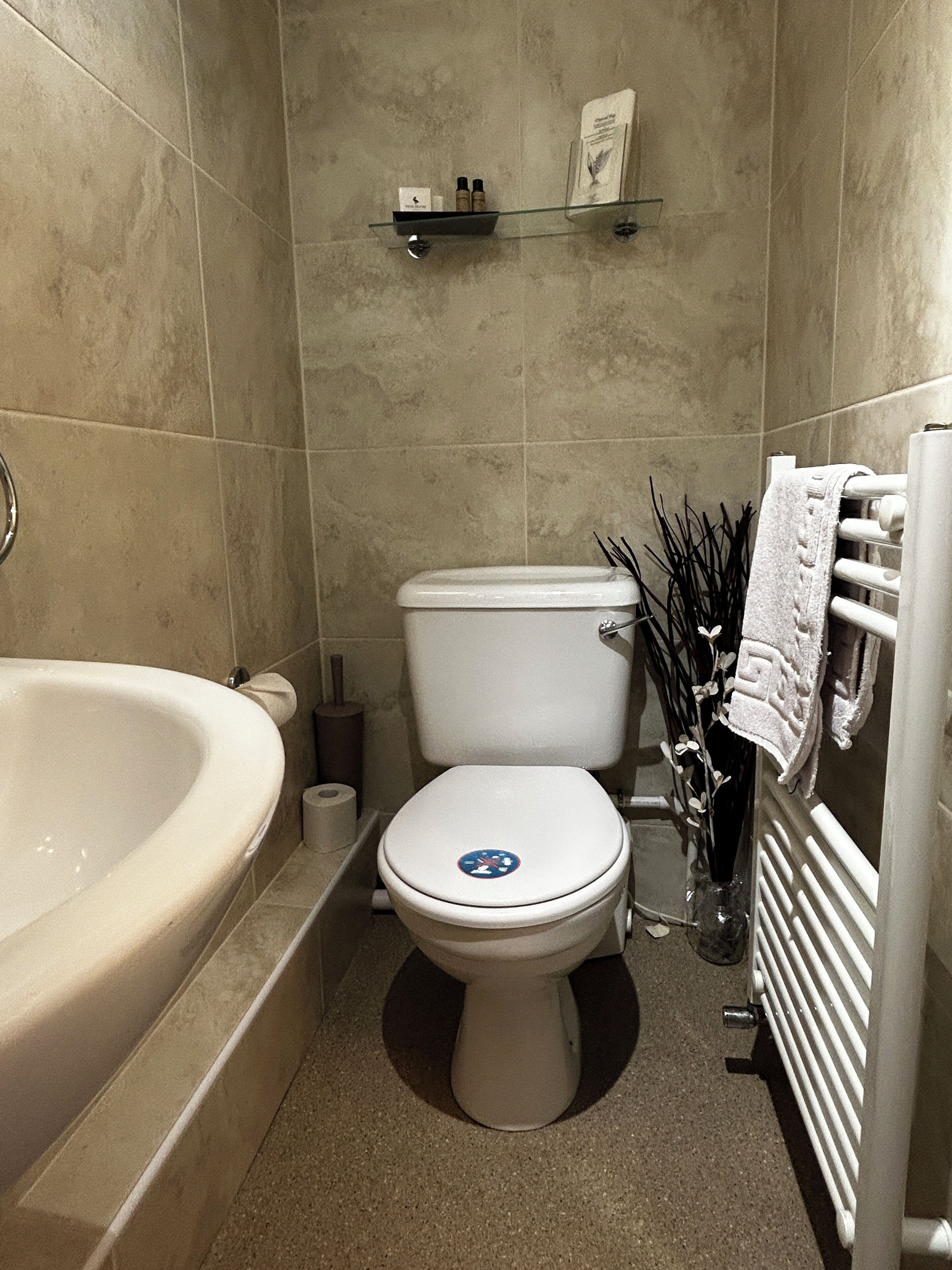 Un baño con bañera, inodoro y estante con artículos de aseo.