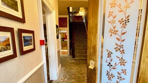 Un pasillo con cuadros en la pared, alfombra estampada y una escalera, además de una puerta con panel decorativo.