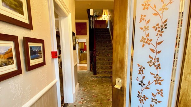 Un pasillo con cuadros en la pared, alfombra estampada y una escalera, además de una puerta con panel decorativo.