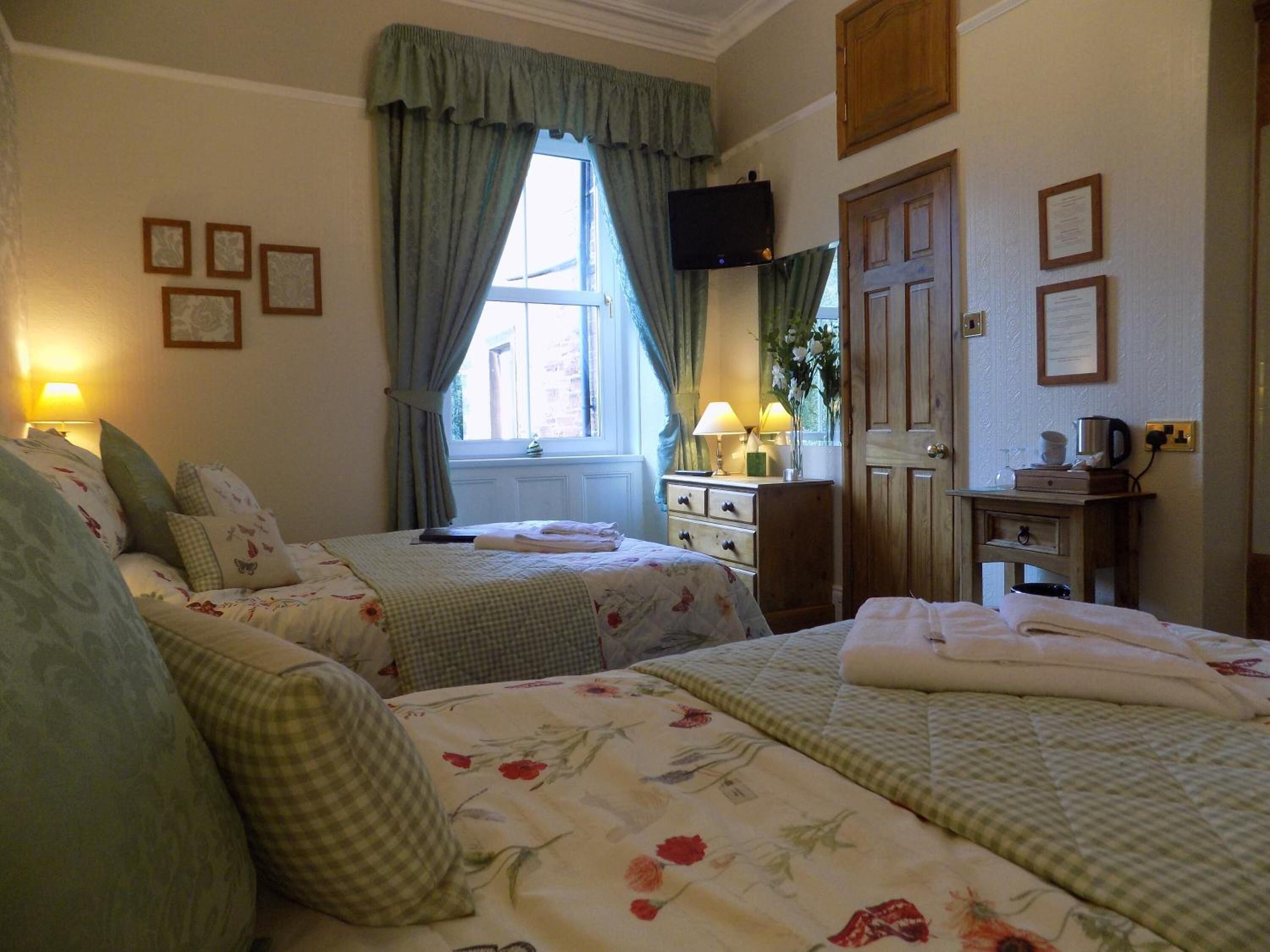 A hotel room with two beds, a television, a dresser, and a window with curtains.