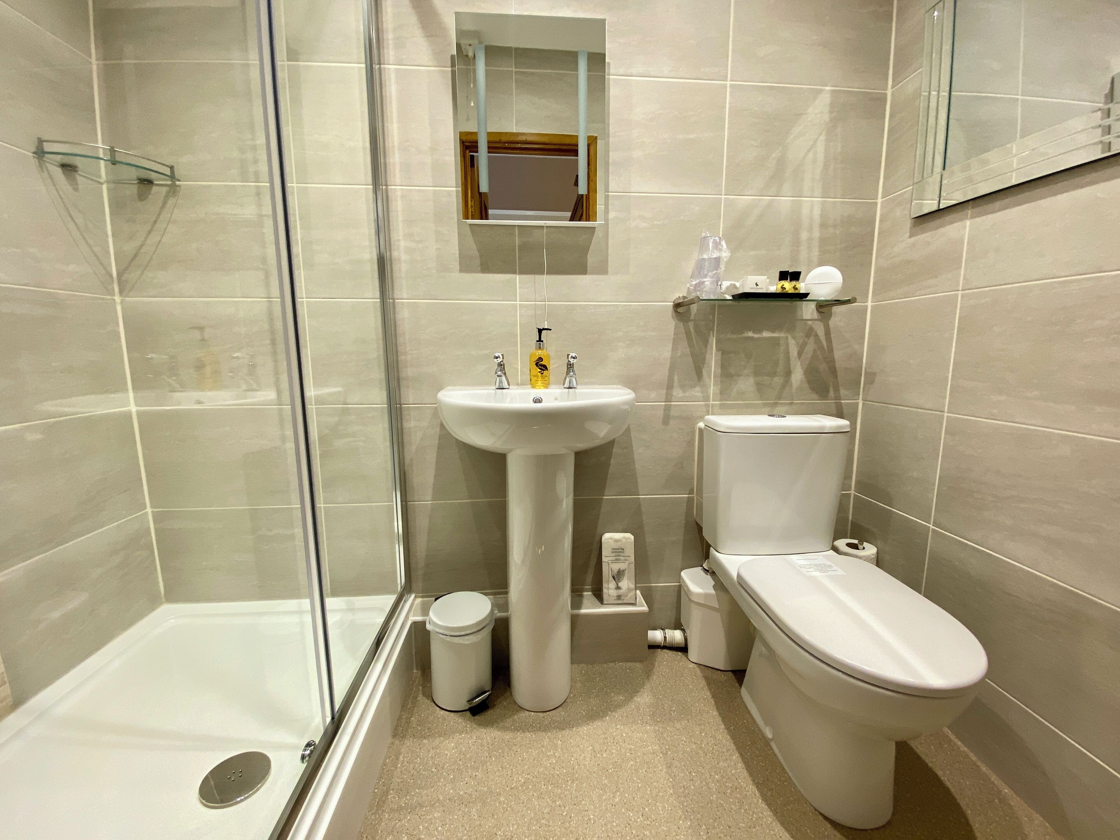 A modern bathroom with a glass shower enclosure, a pedestal sink, a toilet, and a small mirror above the sink.
