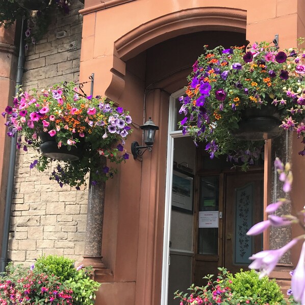 A building entrance with hanging flower baskets and a door with a sign. - Glendale Guest House Penrith (Penrith)