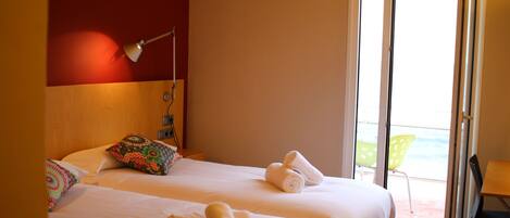 Ein Hotelzimmer mit zwei Betten, einem Schreibtisch, einem Stuhl und einem Balkon mit Meerblick.