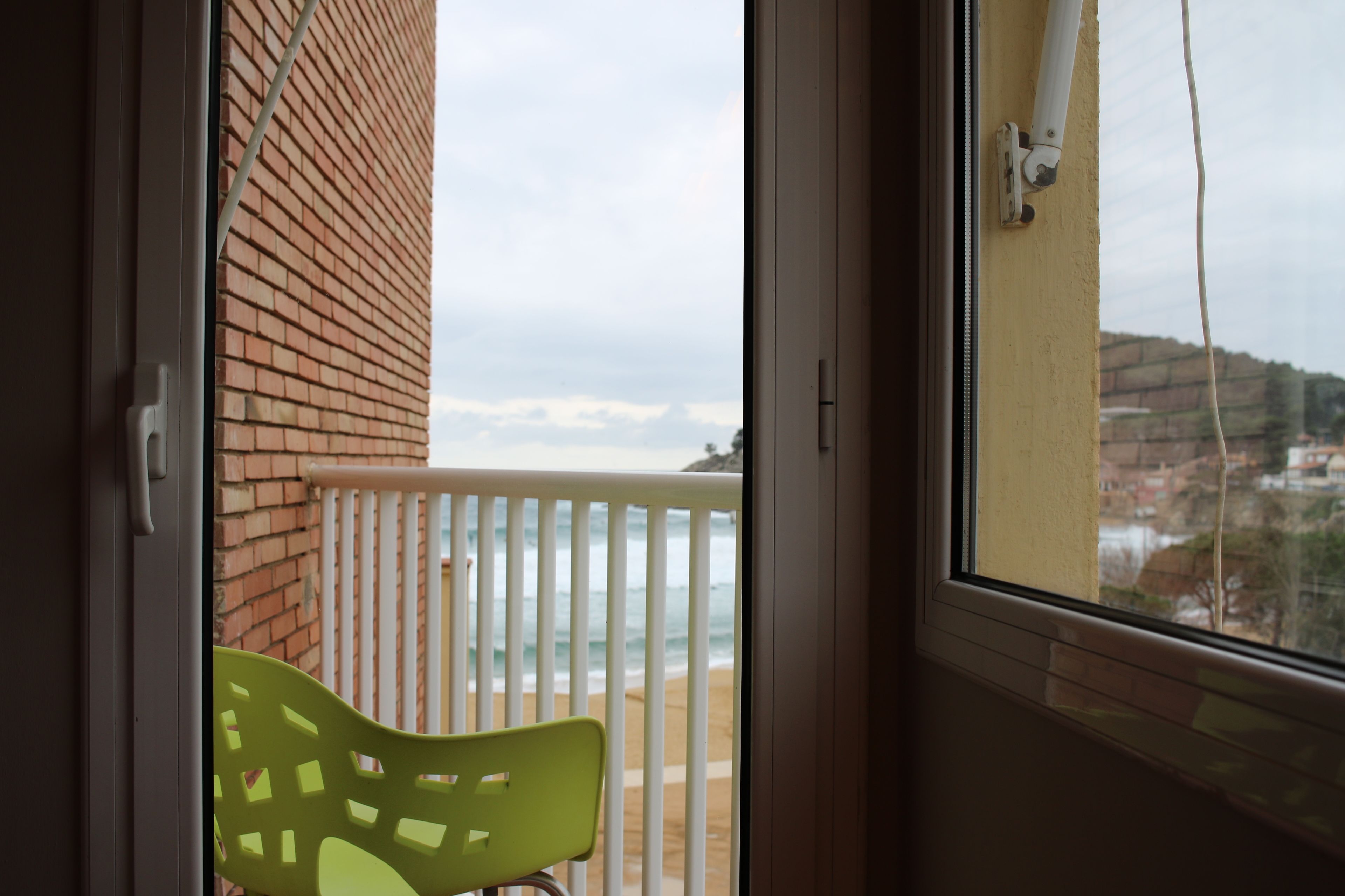 A balcony with a green chair, a white railing, and a view of the beach and buildings.