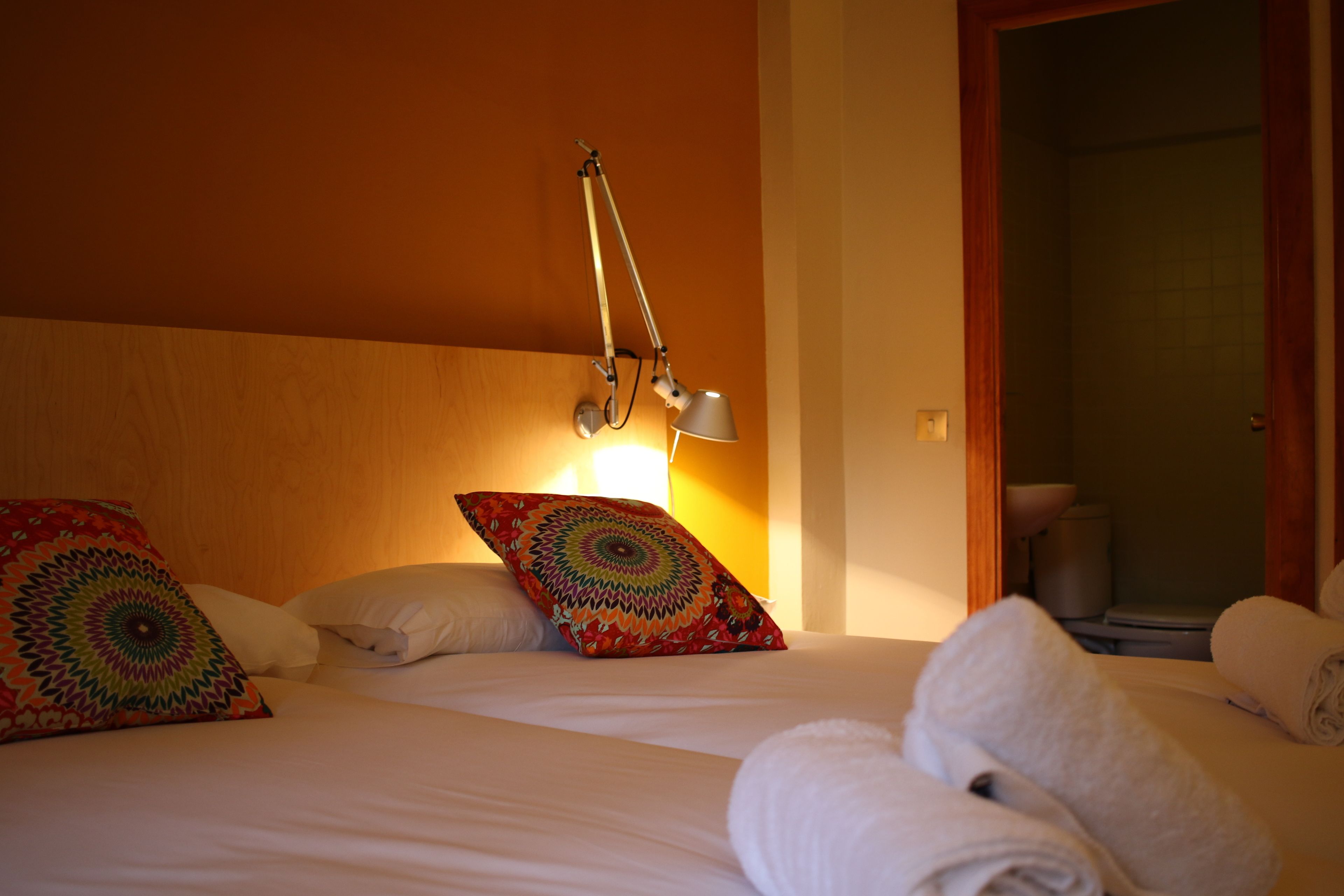 A hotel room with a bed, pillows, a lamp, and a bathroom visible through an open door.