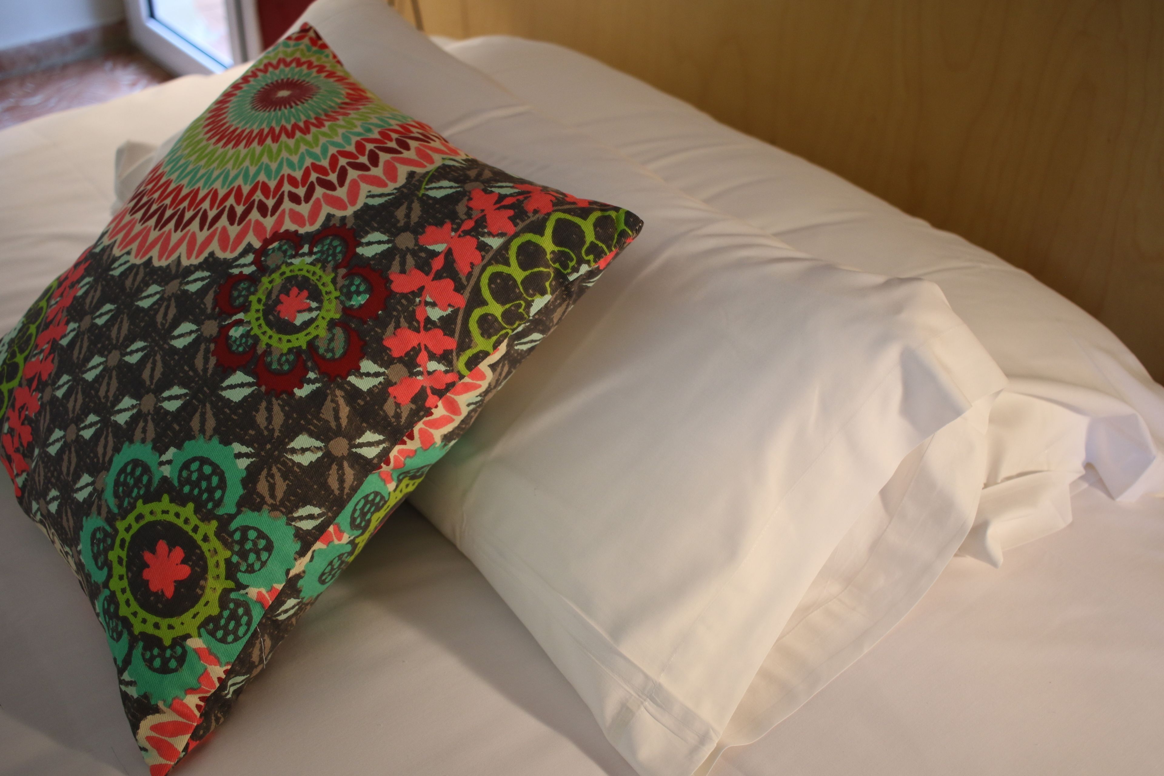 A bed with a colorful patterned pillow and a plain white pillow.