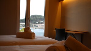 Une chambre d’hôtel avec deux lits, un bureau et une vue sur un plan d’eau et des collines.