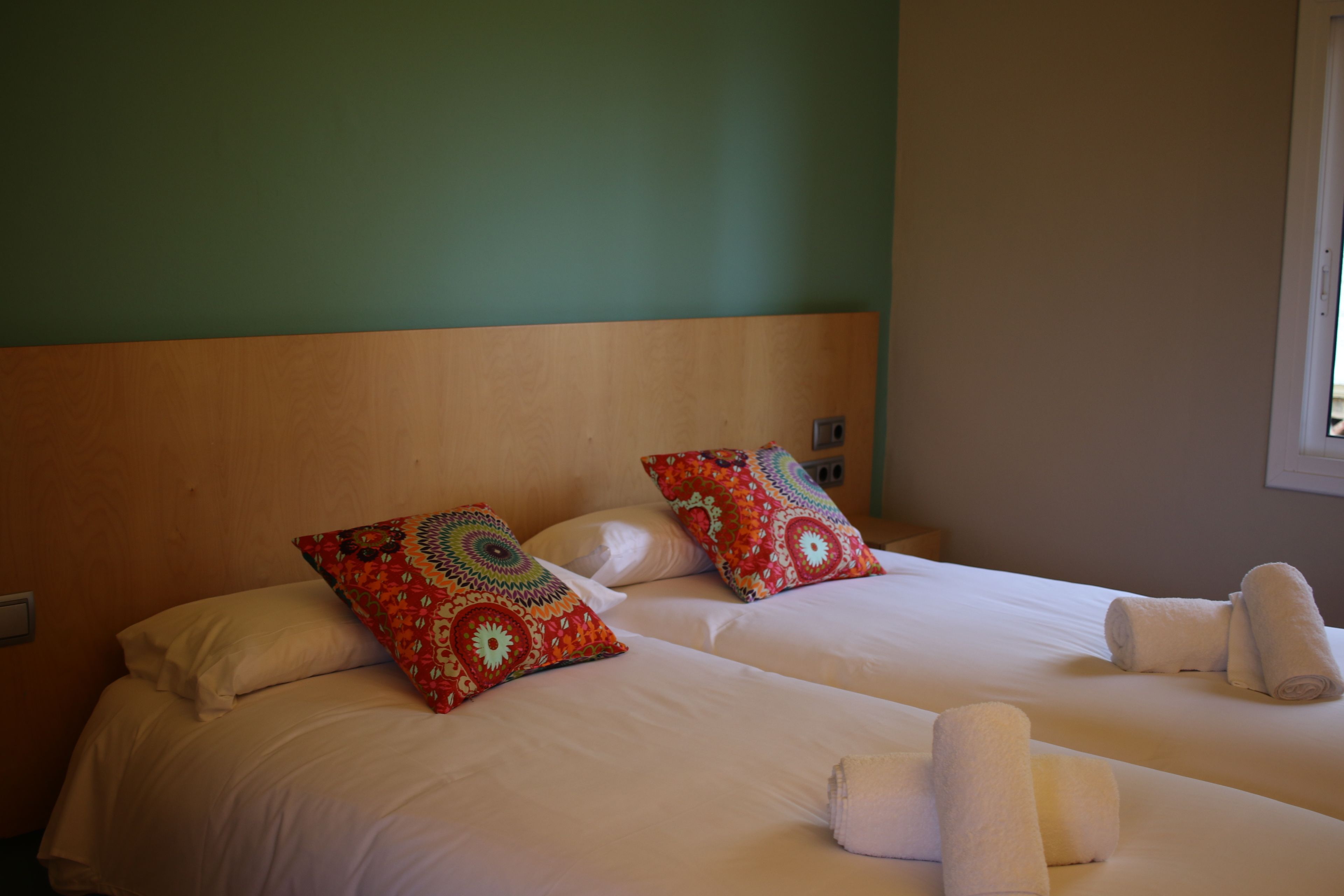 A hotel room with two beds, each with white linens and decorative pillows. There are towels neatly folded on the beds.