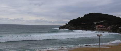 Una playa con olas, una orilla arenosa y una colina con edificios.