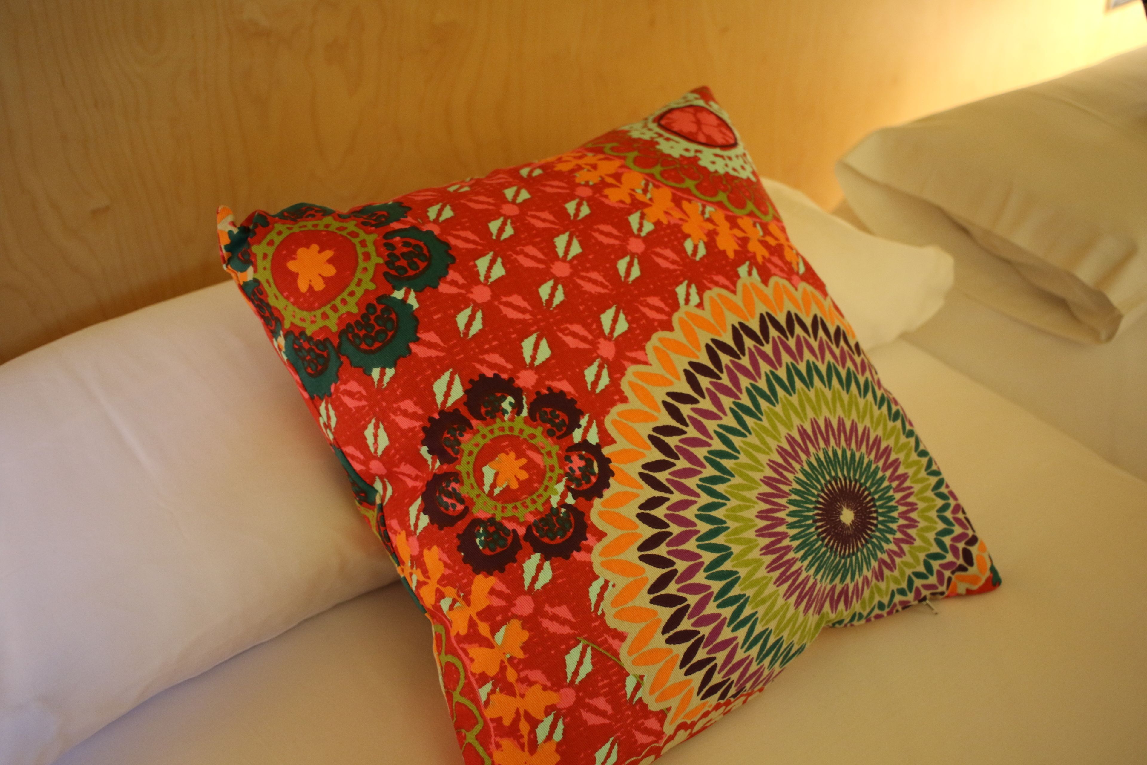 Ein Bett mit einem farbenfrohen, gemusterten Kissen und einem schlichten weißen Kissen.