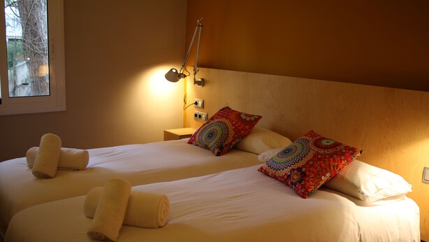 A hotel room with two beds, each with neatly folded towels and colorful patterned pillows. - Hostal LA Fosca (Palamós)