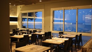 Un restaurant avec des tables dressées, de grandes fenêtres et une vue sur l’extérieur.