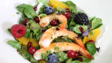 A salad with shrimp, berries, and greens on a white plate.