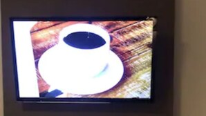A flat-screen TV mounted on a dark wall. Below the TV, there is a wooden shelf with a small white sculpture. - K7 SUITES (Samborondon)
