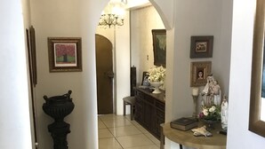 A hallway with a chandelier, a pedestal, framed artwork, and a table with decorative items. - K7 SUITES (Samborondon)