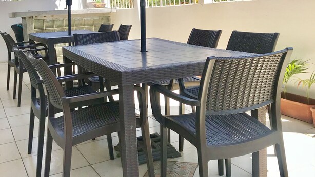 An outdoor patio with a table and chairs, a purple umbrella, and a view of palm trees and buildings. - K7 SUITES (Samborondon)