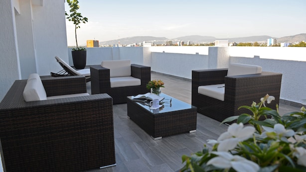 Una terraza en la azotea con mobiliario de mimbre, una mesa de centro de vidrio y una planta en maceta.