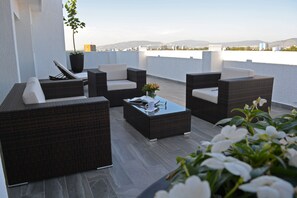 Une terrasse sur le toit, aménagée avec des meubles en osier, une table basse en verre et une plante en pot.