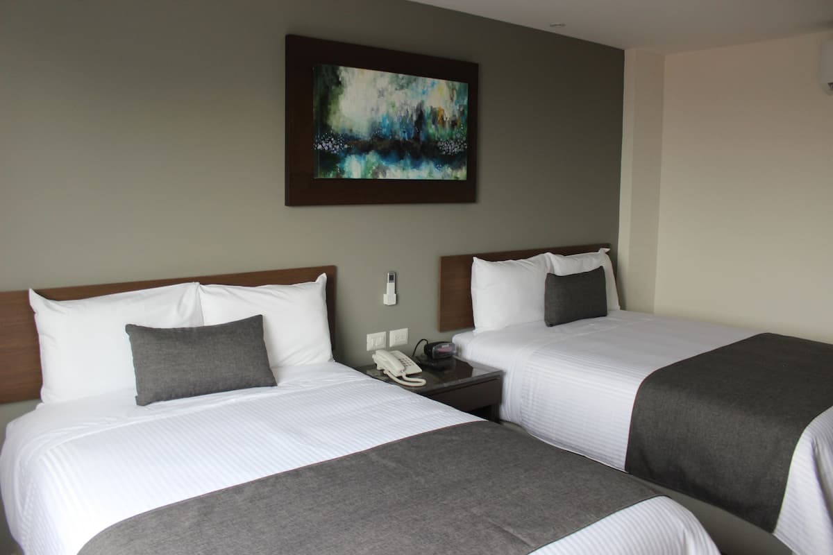 Een hotelkamer met twee bedden, een schilderij aan de muur en een nachtkastje met een telefoon.