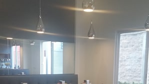 Un restaurante con mesas y sillas de madera, un banco acolchado gris y lámparas colgantes, además de amplias ventanas con vistas al exterior.