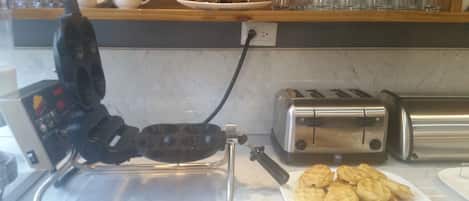 Una cocina con un fabricante de gofres, dos tostadoras y un plato de gofres.