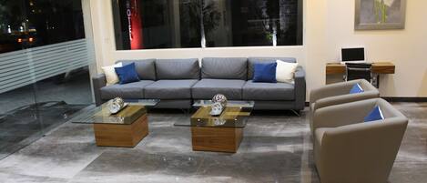 Una sala de estar moderna con un sofá gris, dos mesas de centro de vidrio y un sillón color crema.