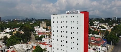 A multi-story building with a red and white facade, labeled "eco HOTEL," surrounded by a cityscape with various buildings and greenery.