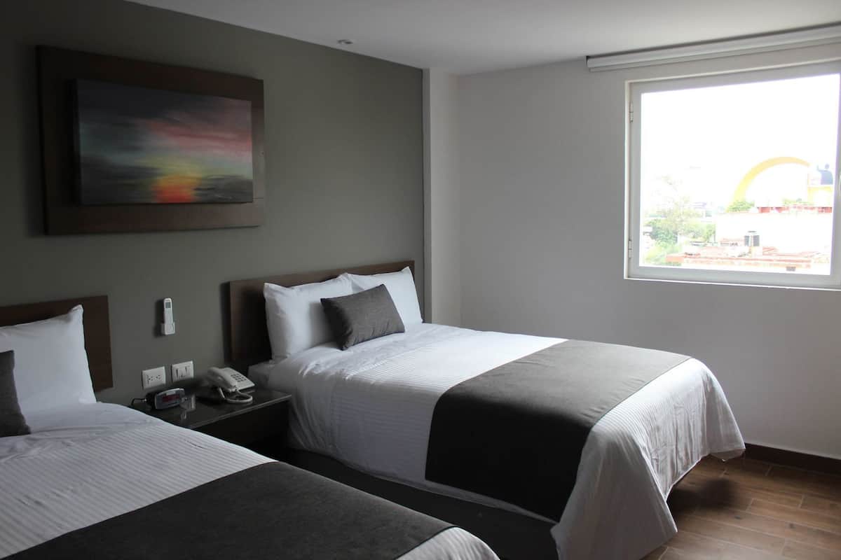 Een hotelkamer met twee bedden, een schilderij aan de muur, een nachtkastje met een telefoon en een raam met uitzicht.