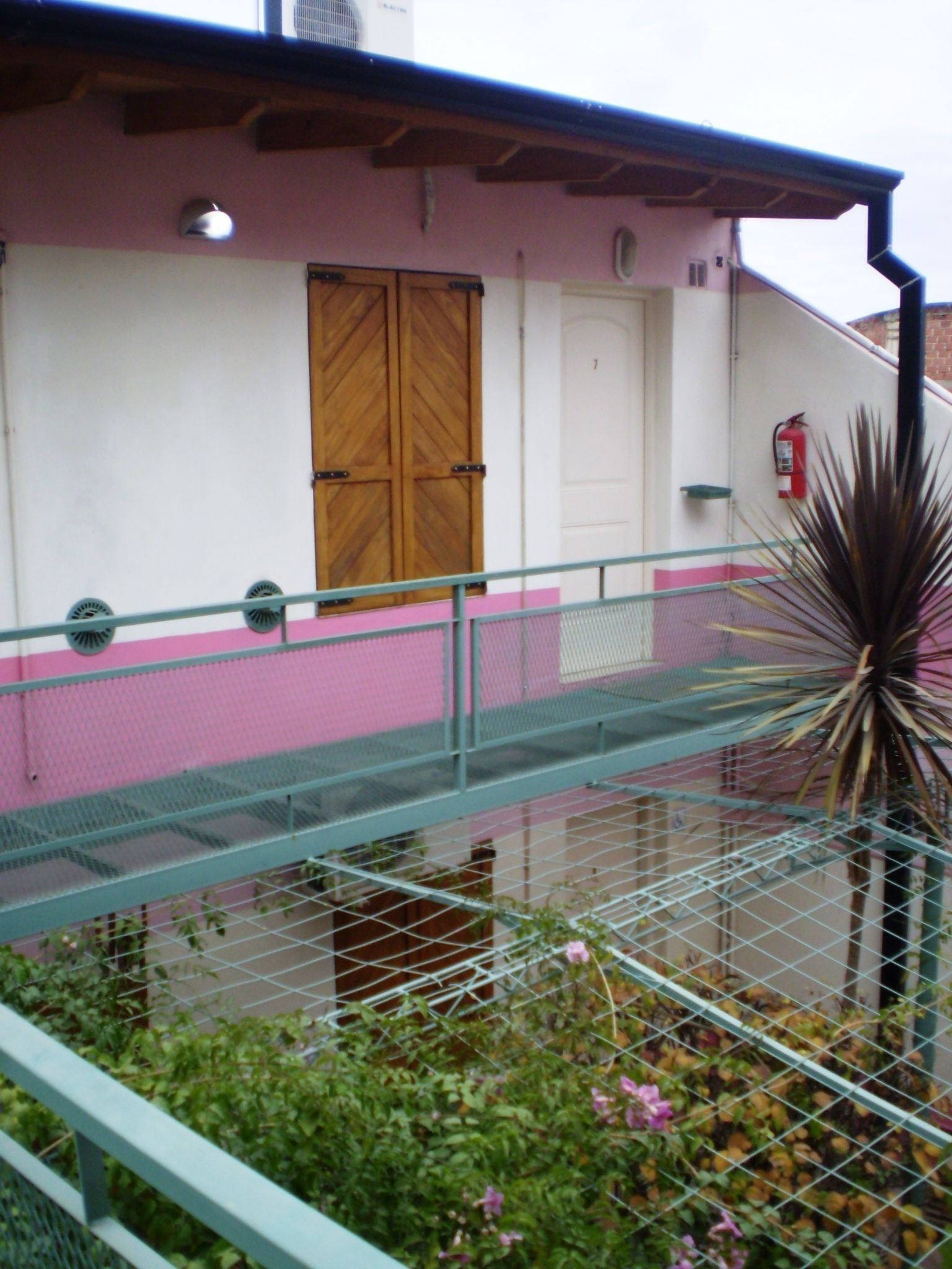 A building with a pink and white facade, a wooden door, a metal railing, and a fire extinguisher.