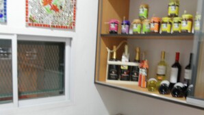 Um quarto pequeno com uma escrivaninha, uma cadeira, uma estante com diversos objetos e uma janela com um adorno.