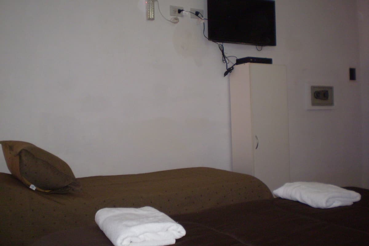 Habitación de hotel con una cama, almohada, toalla doblada, televisor montado en la pared y una puerta.
