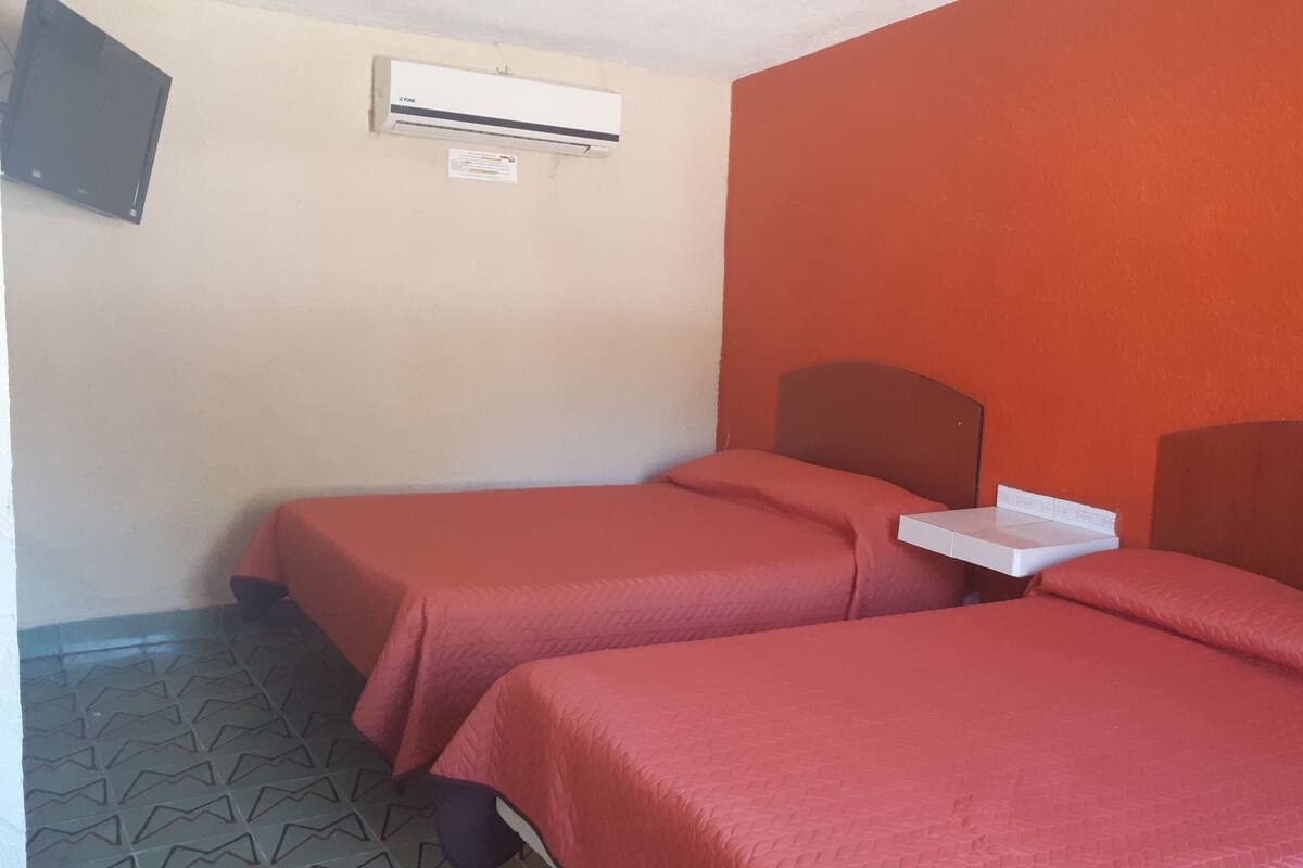 Une chambre avec deux lits, chacun doté d’une tête de lit en bois, d’une petite table et d’un appareil de climatisation fixé au mur.