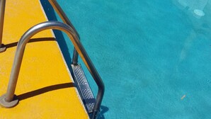 Piscina com borda amarela e escada de metal.