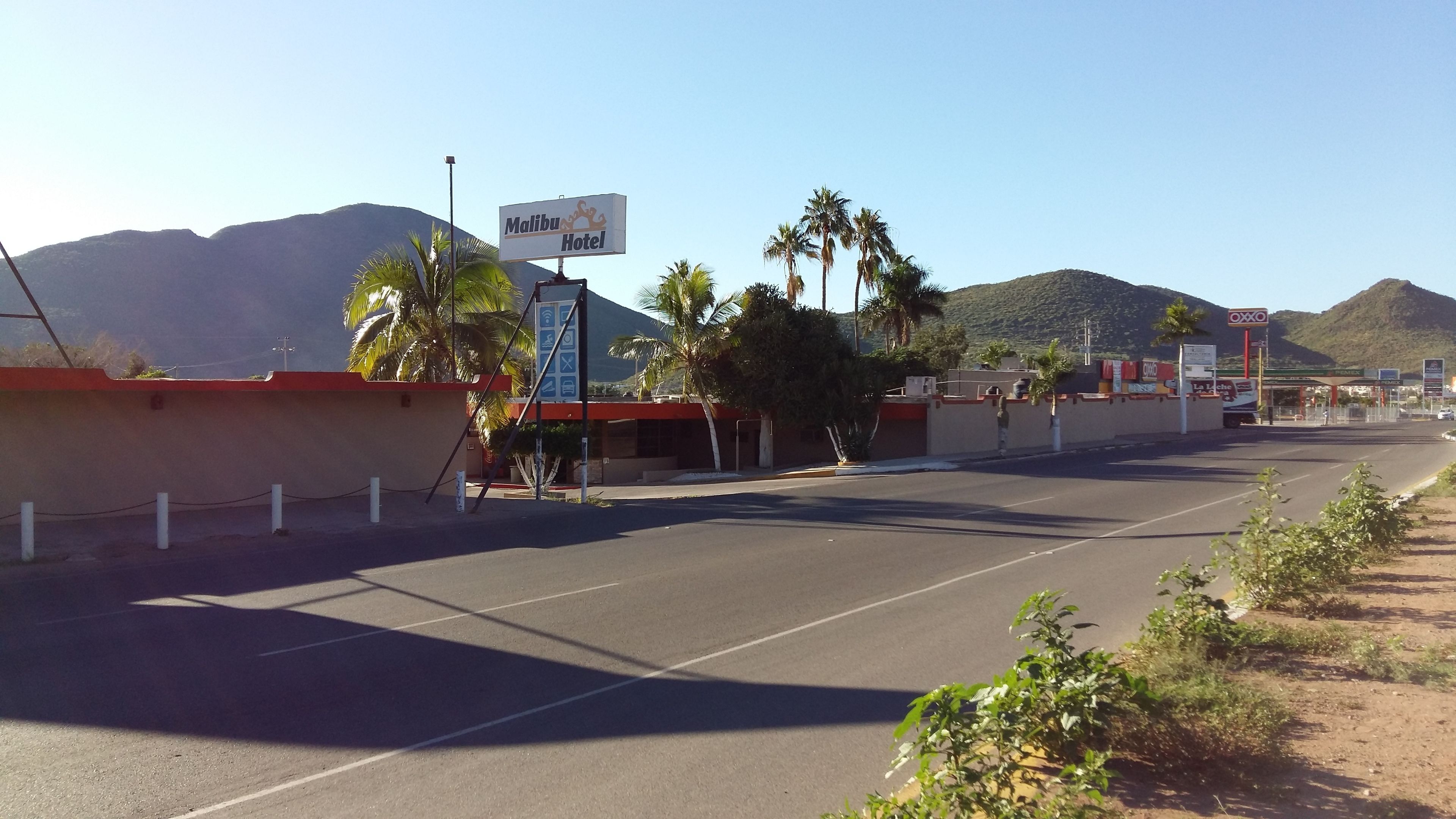 Un estacionamiento con un letrero que indica Malibu Hotel, palmeras y montañas al fondo.