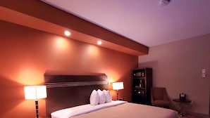 Habitación de hotel con una cama grande, dos lámparas de noche, un cabecero, una mesita con lámpara y una silla.