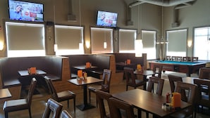 Una sala de billar con mesas y sillas, una mesa de billar y varias pantallas de televisión mostrando noticias.