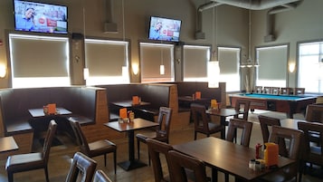 Una sala de billar con mesas y sillas, una mesa de billar y varias pantallas de televisión mostrando noticias.