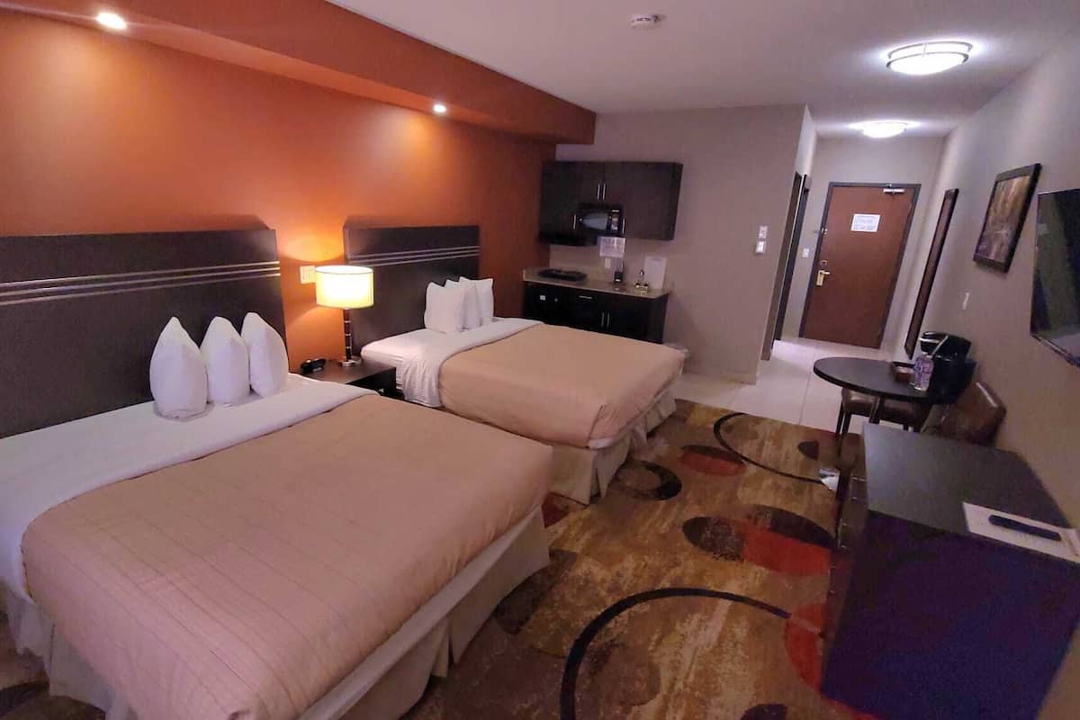A hotel room with two beds, a desk, a TV, and a bathroom door.
